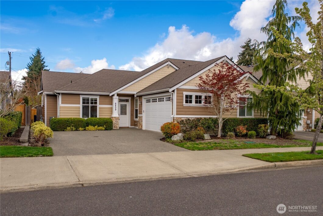 A single-story brick home with a large garage and driveway under a blue sky.