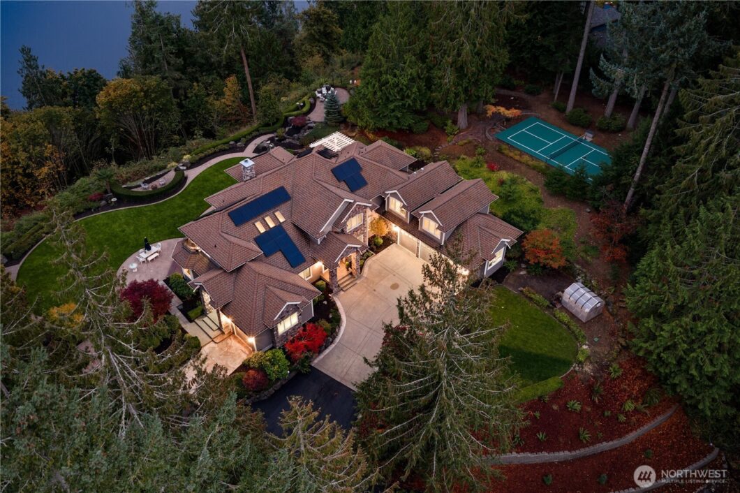 Aerial view of a large house with solar panels on the roof surrounded by trees.