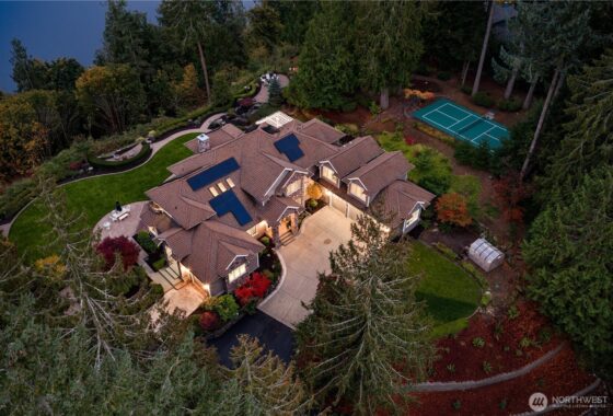 Aerial view of a large house with solar panels on the roof surrounded by trees.