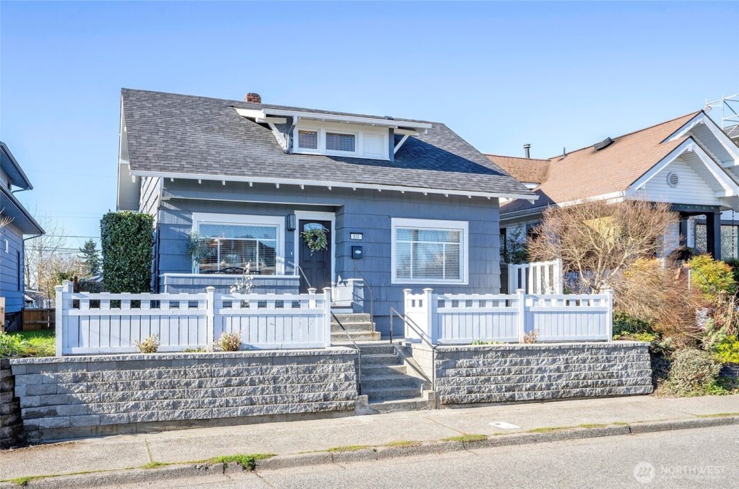 A blue house with white porch railings and a stone retaining wall.
