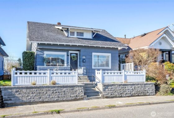 A blue house with white porch railings and a stone retaining wall.
