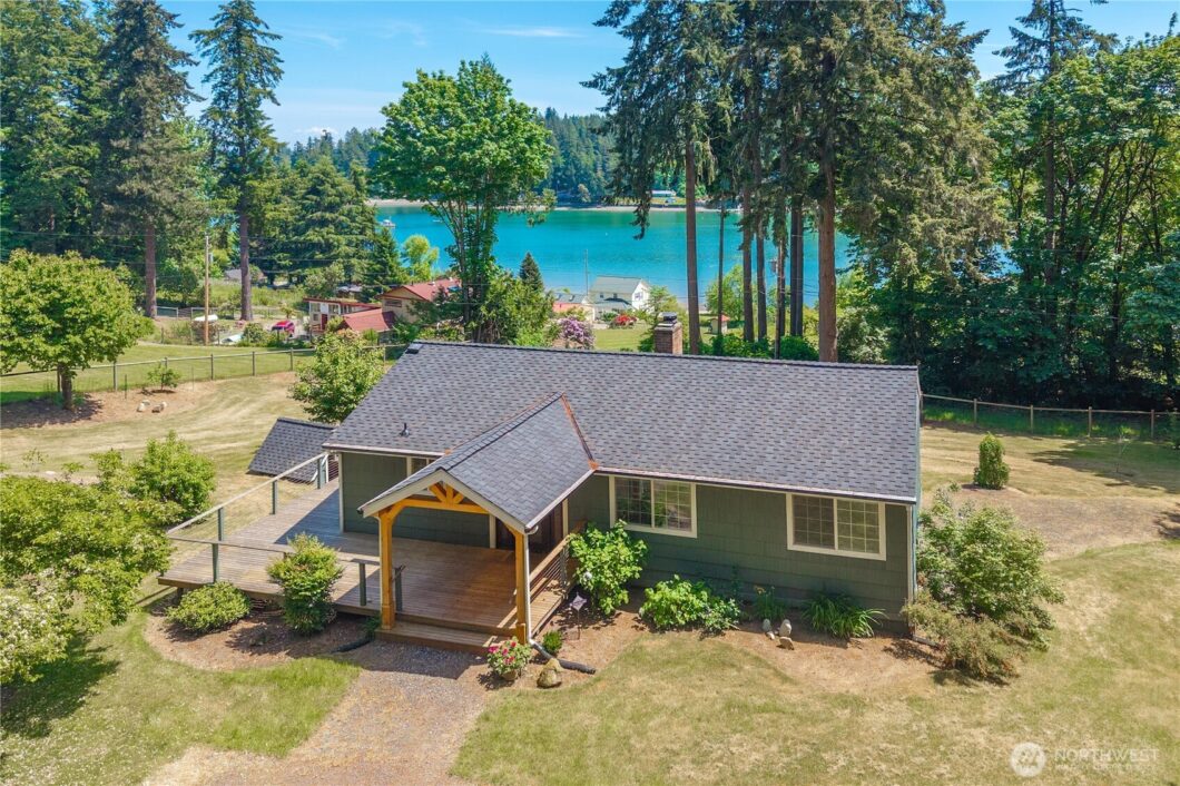 A green house with a covered porch overlooking a blue lake and tall trees.