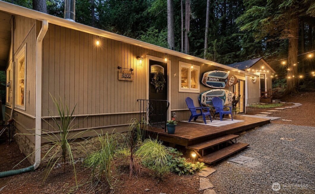 A wooden home exterior with a deck, blue chairs, and warm outdoor lighting.
