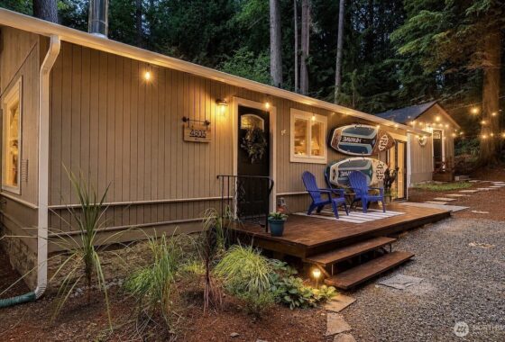 A wooden home exterior with a deck, blue chairs, and warm outdoor lighting.