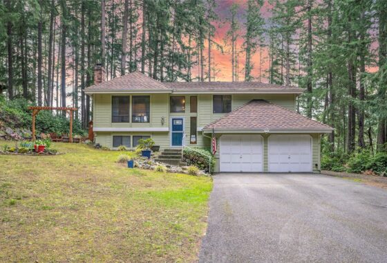 A yellow house with a blue door and white garage set against a backdrop of tall trees.