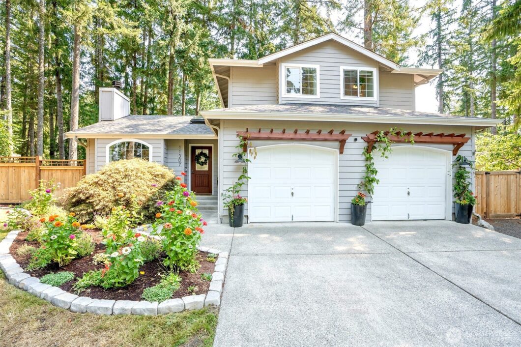 A two-story house with a white garage door, surrounded by greenery and trees.