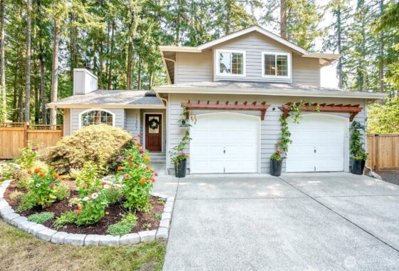 A two-story house with a white garage door, surrounded by greenery and trees.
